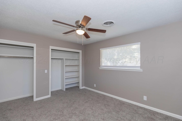 unfurnished bedroom with light carpet, a textured ceiling, two closets, and ceiling fan