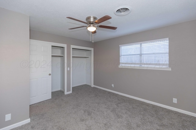 unfurnished bedroom with a textured ceiling, light colored carpet, ceiling fan, and multiple closets