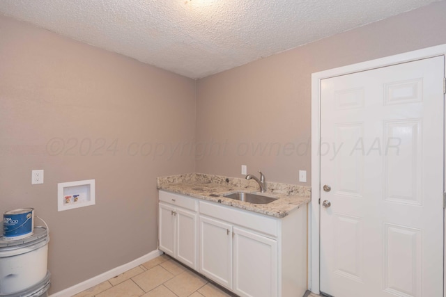 clothes washing area featuring cabinets, hookup for a washing machine, a textured ceiling, sink, and light tile patterned flooring