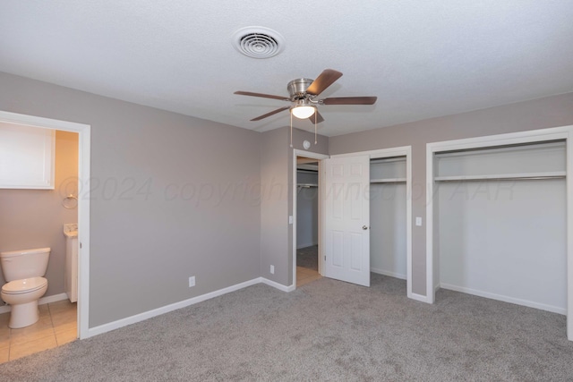 unfurnished bedroom featuring connected bathroom, ceiling fan, light carpet, and two closets