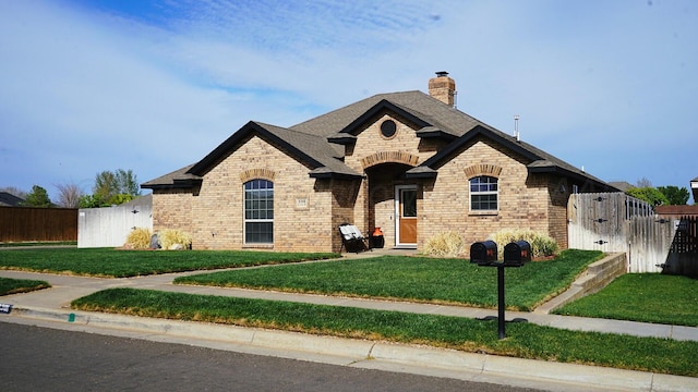 french country inspired facade with a front lawn, a gate, a chimney, fence, and brick siding
