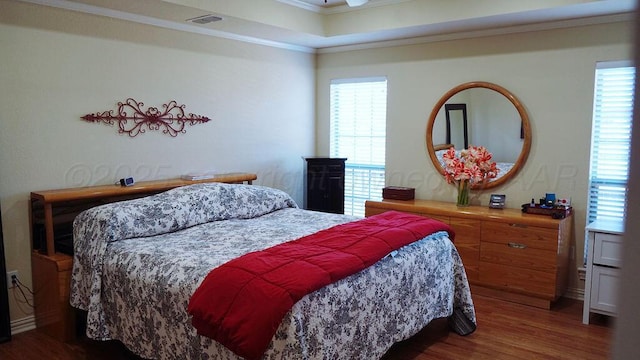 bedroom featuring visible vents, wood finished floors, ornamental molding, and a tray ceiling