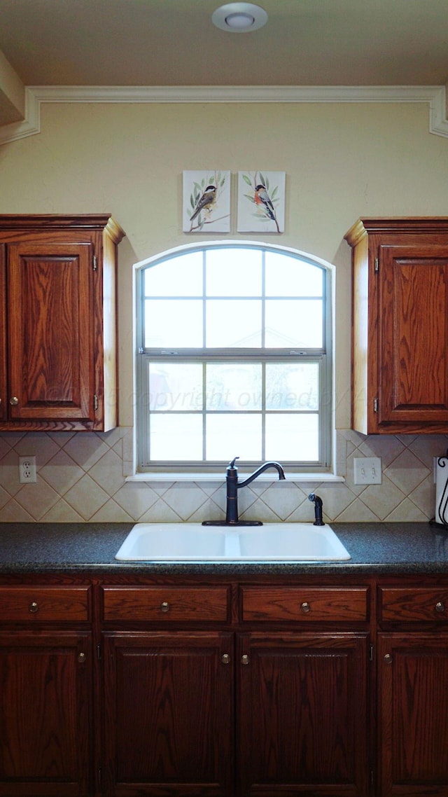 kitchen with dark countertops, crown molding, a sink, and a healthy amount of sunlight