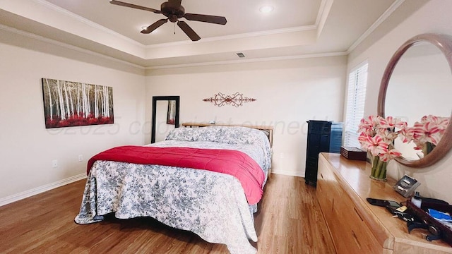 bedroom featuring baseboards, crown molding, wood finished floors, and a raised ceiling