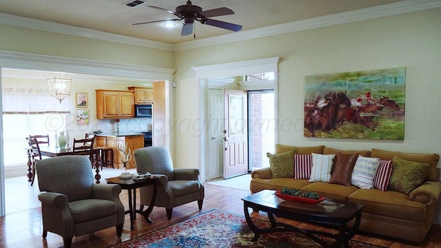 living room featuring light wood-type flooring, a ceiling fan, visible vents, and ornamental molding