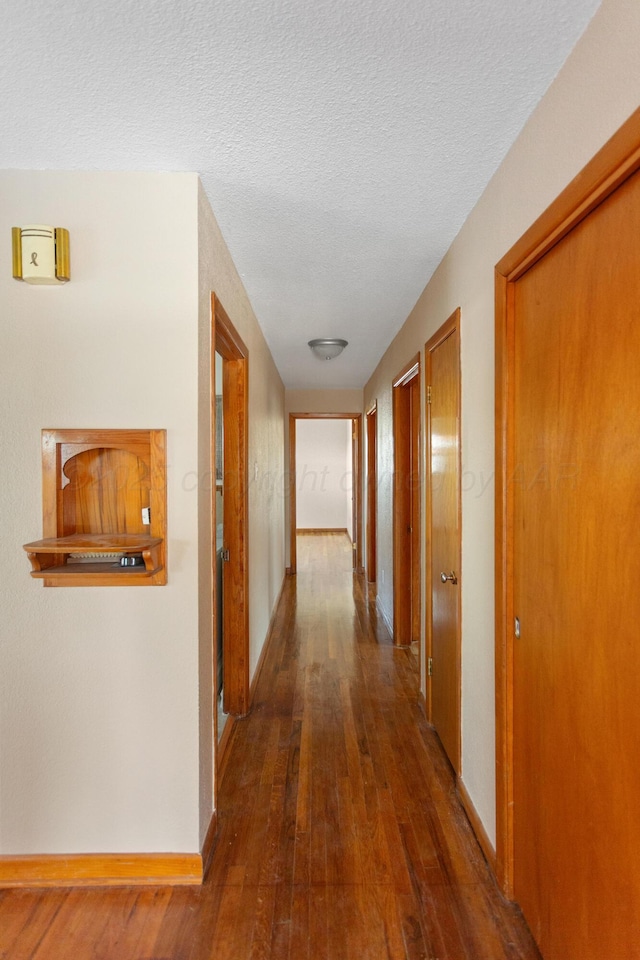 corridor with baseboards, dark wood finished floors, and a textured ceiling