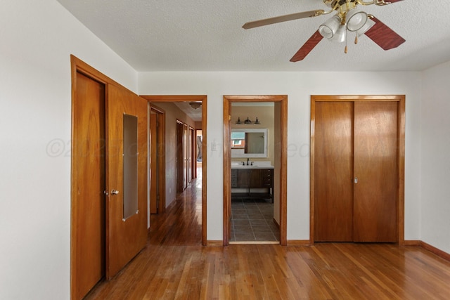 unfurnished bedroom with multiple closets, a textured ceiling, baseboards, and wood finished floors