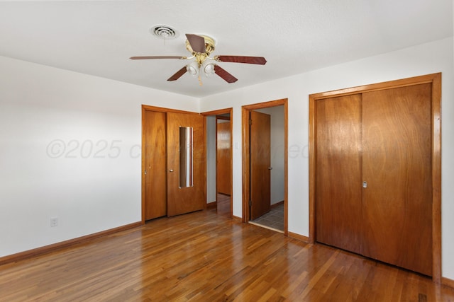 unfurnished bedroom with two closets, visible vents, ceiling fan, wood finished floors, and baseboards