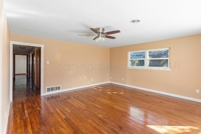 empty room with a ceiling fan, visible vents, dark wood finished floors, and baseboards