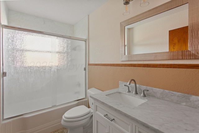 bathroom with toilet, a textured wall, enclosed tub / shower combo, and vanity