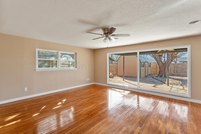 unfurnished room featuring plenty of natural light, wood finished floors, visible vents, and baseboards