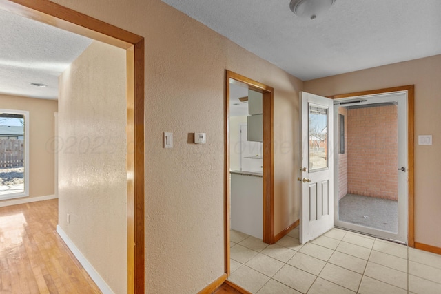 hall featuring light tile patterned floors, baseboards, a textured ceiling, and a textured wall