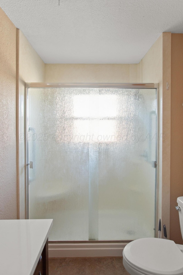 bathroom featuring toilet, tile patterned floors, a textured ceiling, vanity, and a shower stall