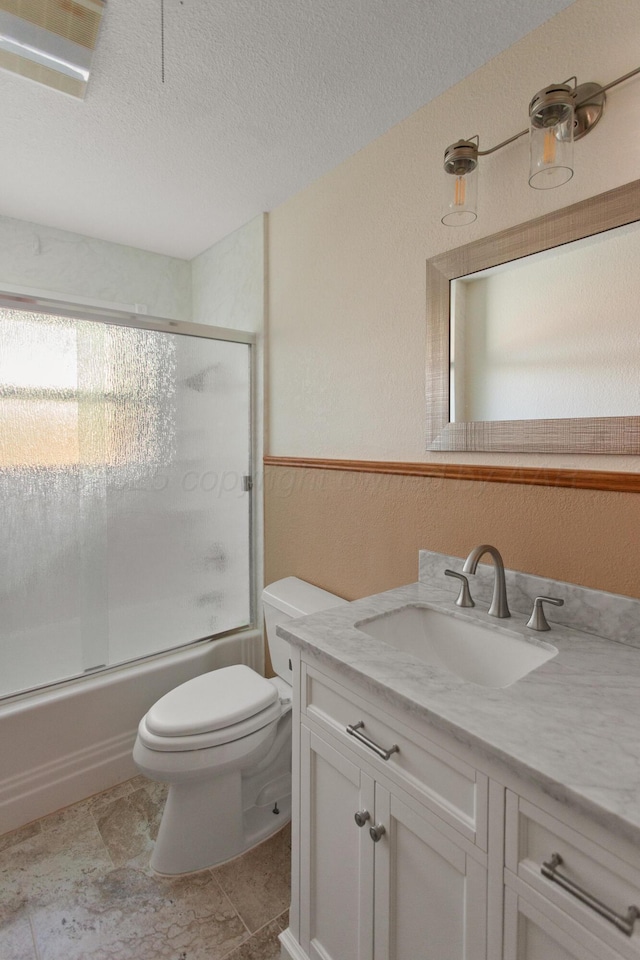 bathroom with a textured wall, toilet, combined bath / shower with glass door, a textured ceiling, and vanity