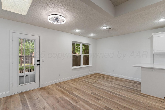 2607 15th Ave, Canyon, TX 79015 - unfurnished dining area with a textured ceiling, light wood-style flooring, plenty of natural light, baseboards, and a skylight