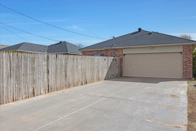 view of property exterior featuring brick siding, driveway, and fence