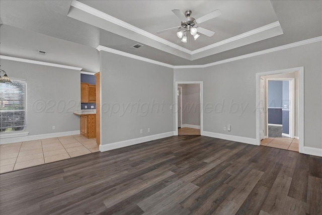 empty room featuring visible vents, ceiling fan, ornamental molding, wood finished floors, and a raised ceiling