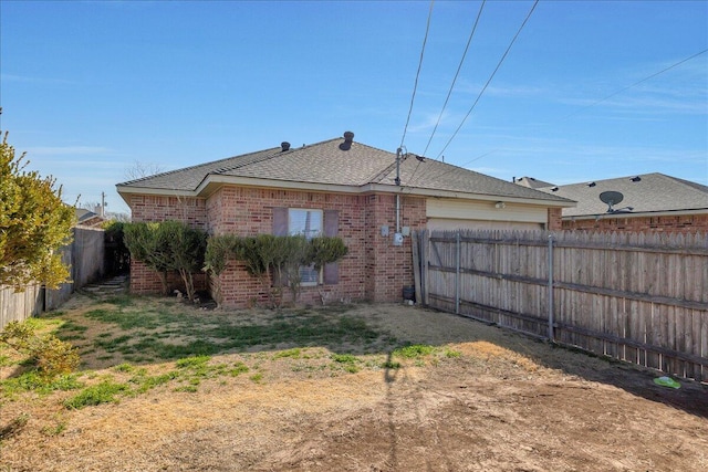 rear view of house with brick siding, a fenced backyard, and a garage