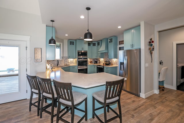 kitchen featuring tasteful backsplash, custom exhaust hood, stainless steel appliances, dark hardwood / wood-style floors, and hanging light fixtures