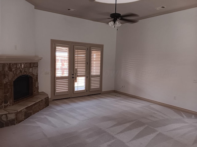 unfurnished living room featuring visible vents, light carpet, ceiling fan, a stone fireplace, and baseboards