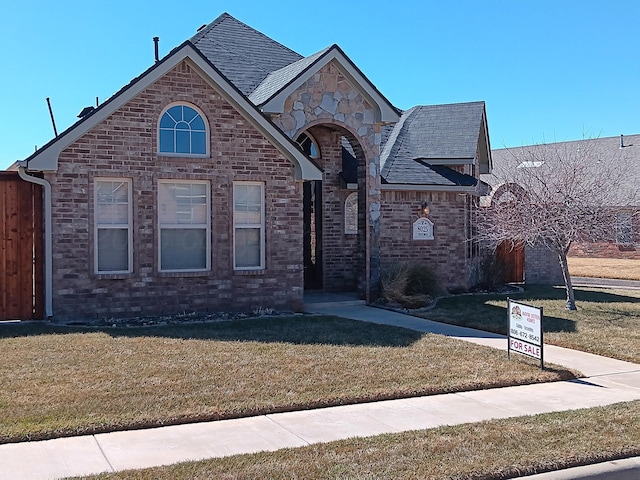 view of front of house with brick siding, roof with shingles, and a front yard