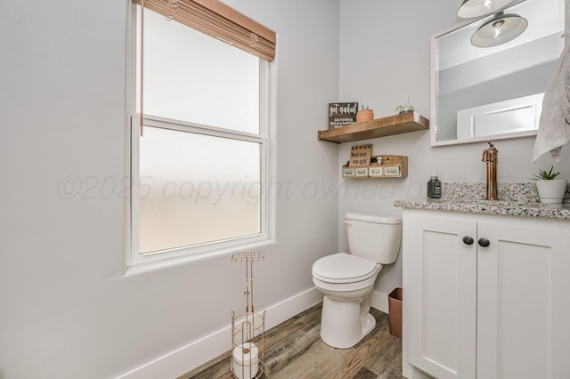 half bathroom with wood finished floors, vanity, toilet, and baseboards