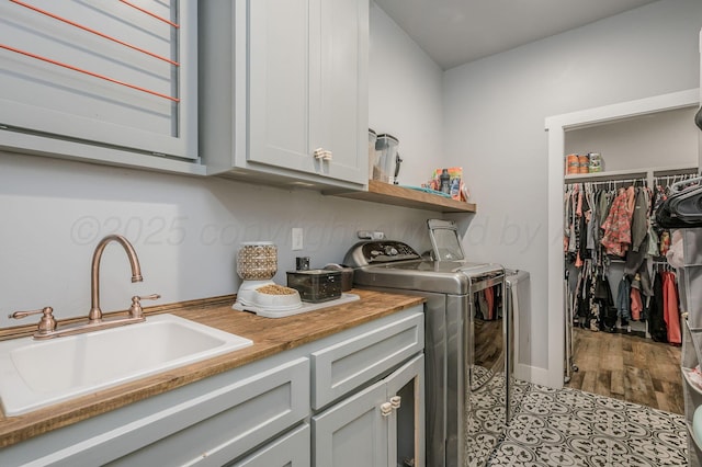 clothes washing area with cabinet space, independent washer and dryer, wood finished floors, and a sink