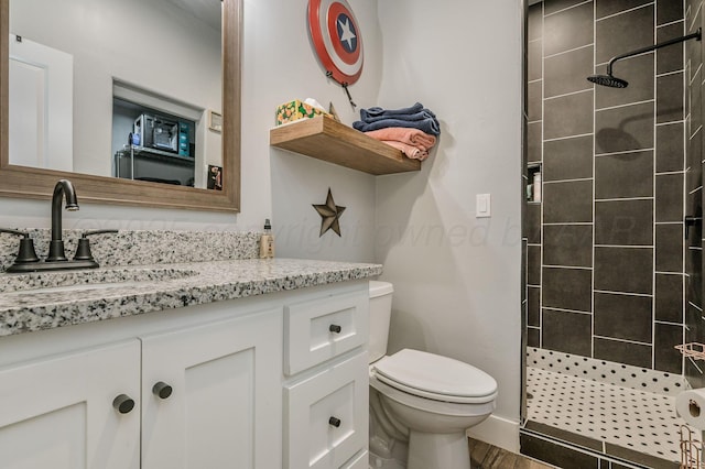 full bath with toilet, vanity, wood finished floors, and tiled shower