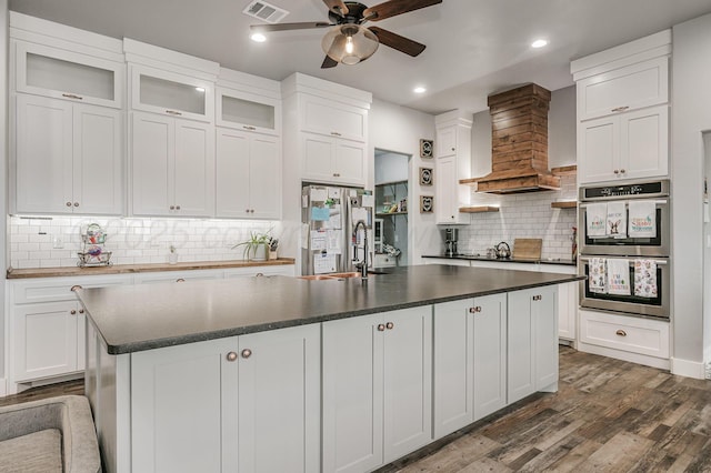 kitchen with a ceiling fan, dark countertops, double oven, dark wood-style flooring, and visible vents
