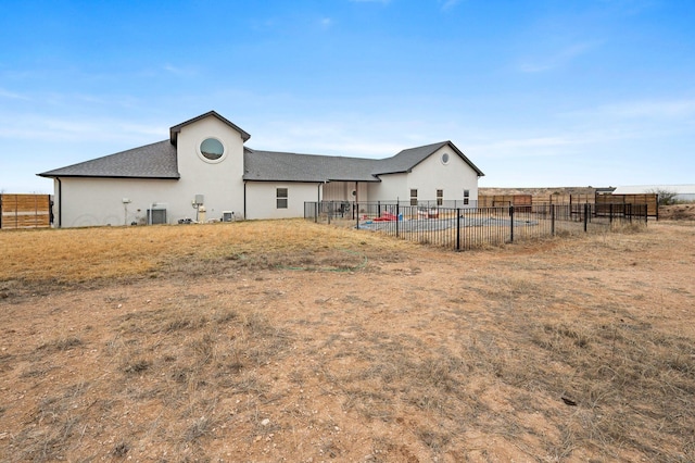 rear view of property featuring fence, roof with shingles, central AC, and stucco siding