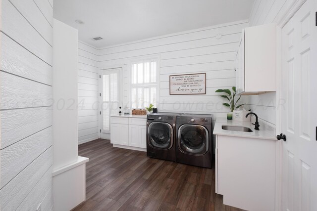 laundry area featuring dark hardwood / wood-style flooring, cabinets, wooden walls, sink, and washing machine and clothes dryer