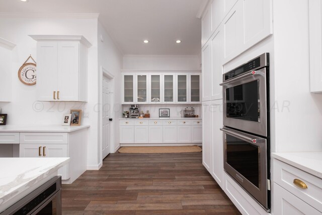 kitchen with white cabinetry, dark wood-type flooring, light stone counters, and stainless steel double oven