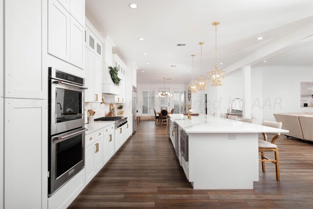 kitchen featuring dark wood-type flooring, hanging light fixtures, white cabinetry, appliances with stainless steel finishes, and a large island with sink