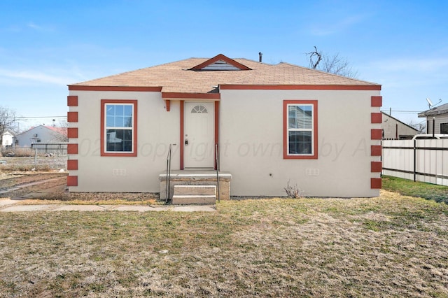 bungalow-style house featuring roof with shingles, fence, a front lawn, and stucco siding