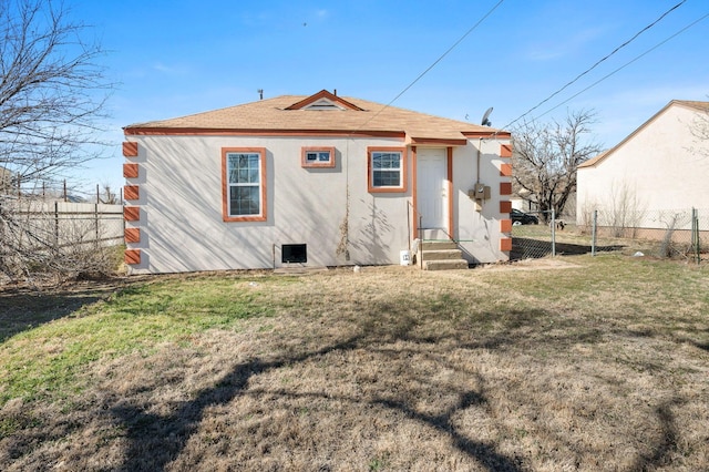 rear view of house with entry steps, a yard, fence, and stucco siding