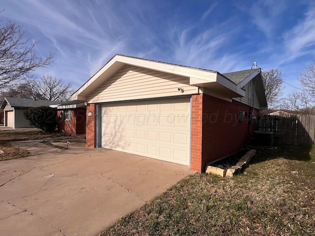 view of home's exterior with fence, concrete driveway, a garage, brick siding, and central AC unit