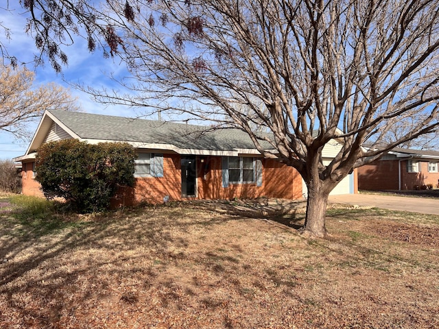 ranch-style house with brick siding, concrete driveway, a front lawn, and roof with shingles