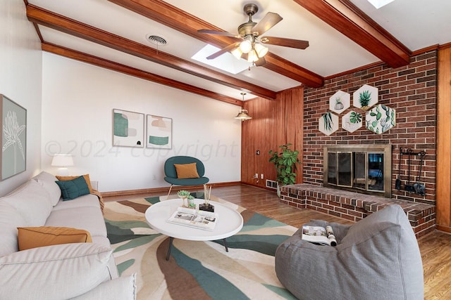 living room with ceiling fan, light hardwood / wood-style floors, ornamental molding, a fireplace, and beam ceiling