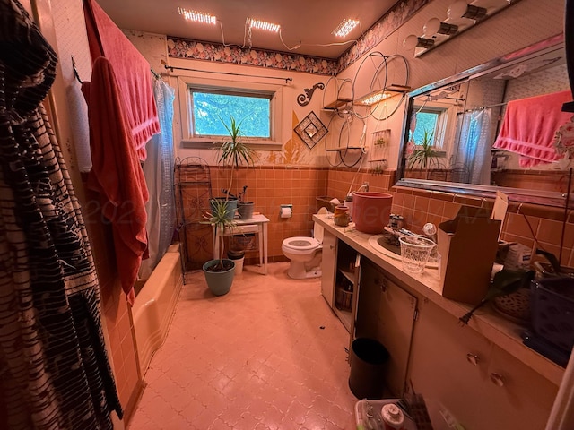 209 N Bowie Ave, Tulia, TX 79088 - full bathroom featuring wallpapered walls, tile walls, shower / tub combo with curtain, vanity, and wainscoting