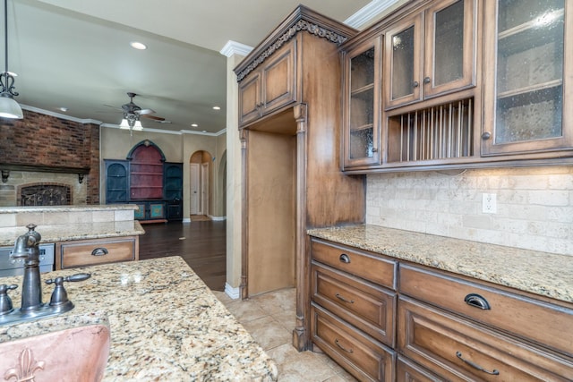 kitchen featuring brown cabinets, light stone countertops, arched walkways, a ceiling fan, and ornamental molding