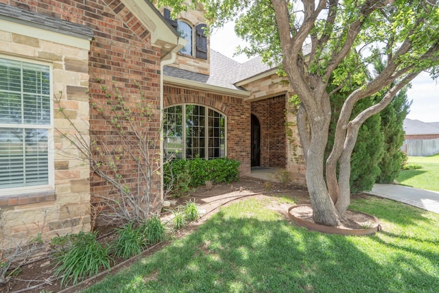 entrance to property with a yard, brick siding, stone siding, and roof with shingles
