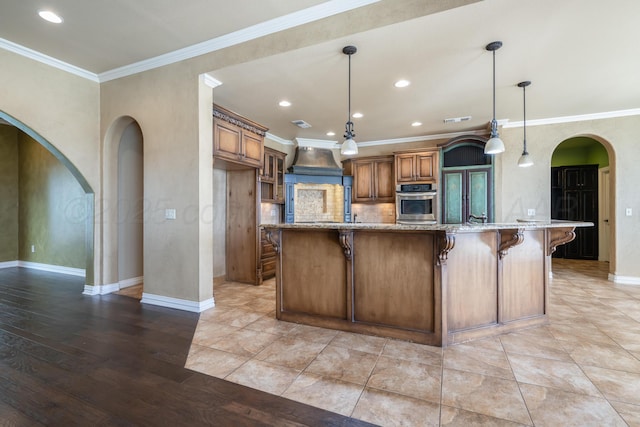 kitchen with brown cabinetry, arched walkways, light stone countertops, baseboards, and stainless steel oven