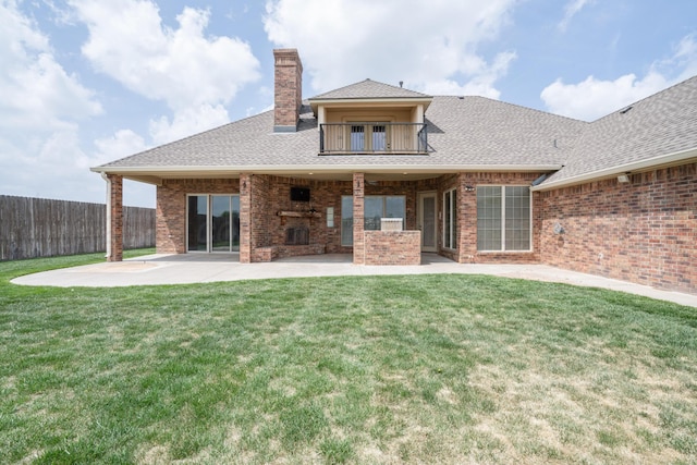 rear view of house with fence, brick siding, a balcony, a lawn, and a patio