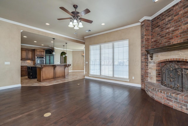 unfurnished living room with crown molding, ceiling fan, a fireplace, baseboards, and hardwood / wood-style flooring