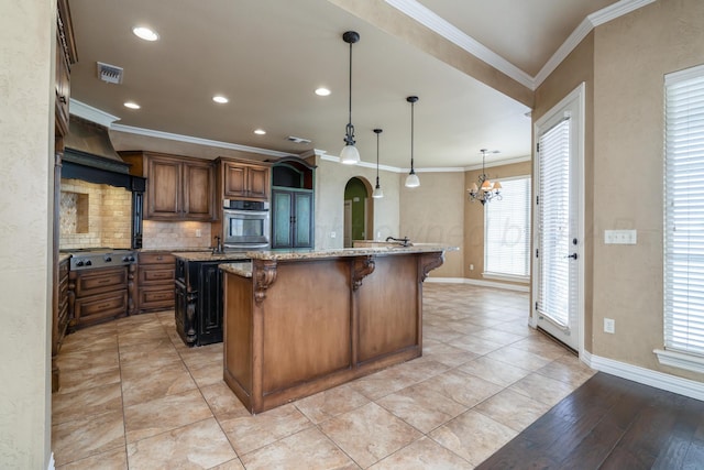 kitchen with an island with sink, a breakfast bar area, arched walkways, appliances with stainless steel finishes, and backsplash