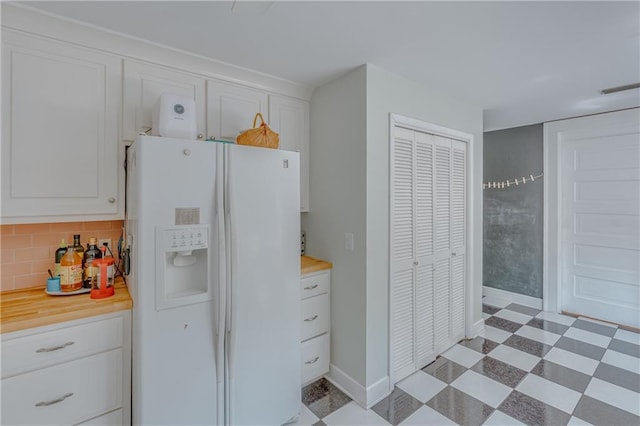 kitchen featuring light floors, white refrigerator with ice dispenser, light countertops, white cabinetry, and backsplash