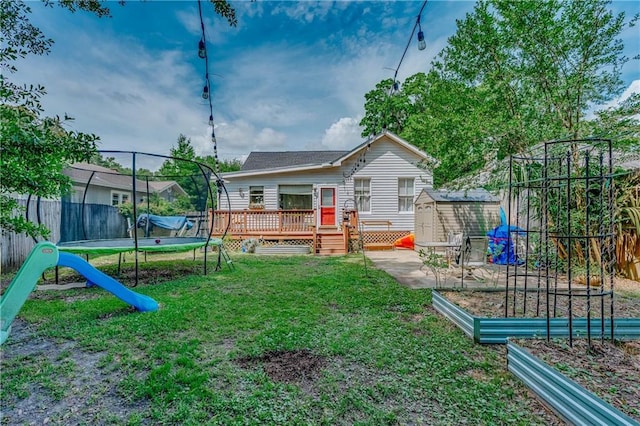 view of playground with an outdoor structure, a deck, a vegetable garden, a trampoline, and a storage shed