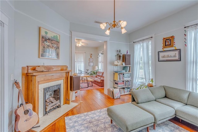 living area featuring an inviting chandelier, light wood-type flooring, a tile fireplace, and a wealth of natural light