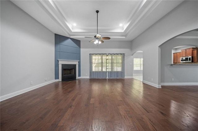 unfurnished living room featuring dark wood-type flooring, ceiling fan, ornamental molding, and a raised ceiling