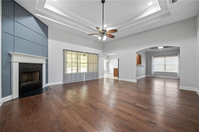 unfurnished living room featuring dark hardwood / wood-style flooring, ceiling fan, ornamental molding, a tiled fireplace, and a raised ceiling